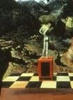 Detail: a small dark upright figure standing on a red pedestal above a checkered floor, in the middle distance of the painting