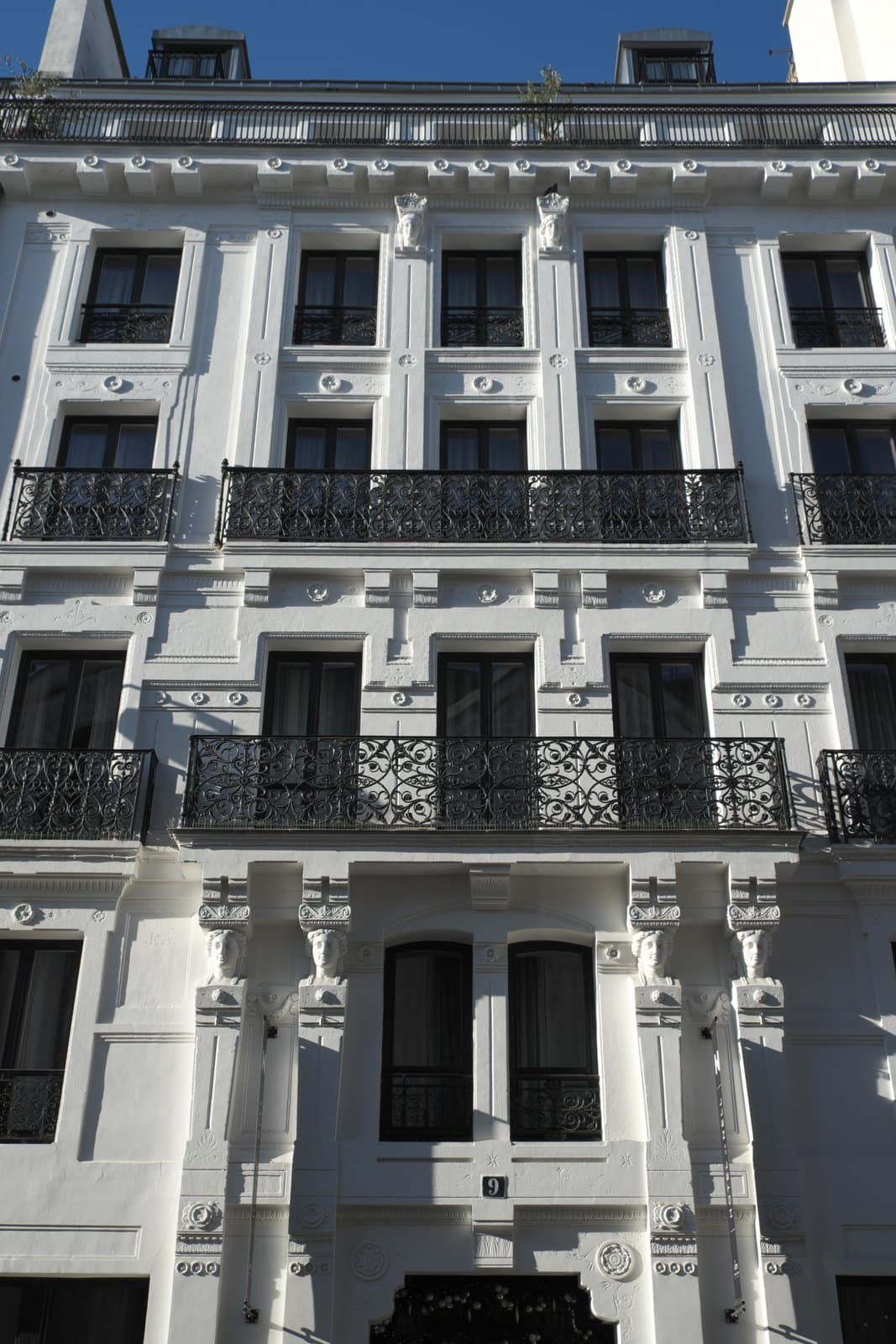 Photograph of the white façade of 9 rue du Conservatoire, five windows wide, with wrought-iron balconies and carved busts beside the first-floor windows.