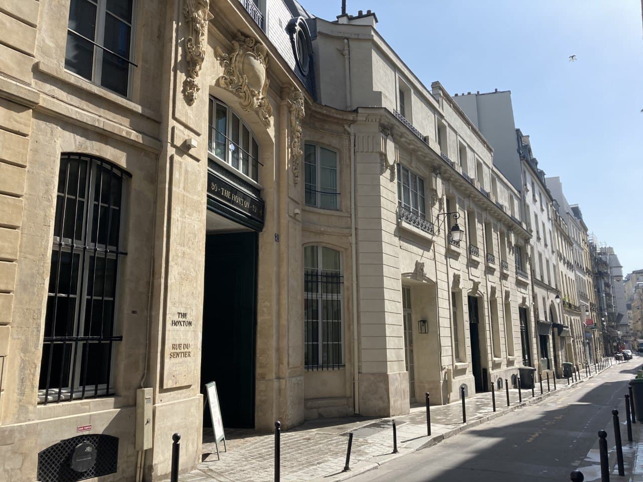 Photograph of the carved stone entrance of The Hoxton on rue du Sentier, with a sign reading 30 The Hoxton 32 above the carriage door and the narrow street running away to the right.