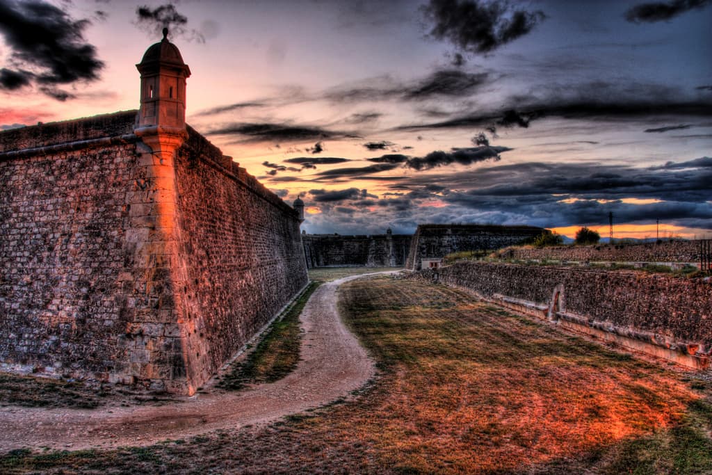 Stone bastions, defensive walls, and a dry moat at Sant Ferran Castle in Figueres under a dramatic evening sky