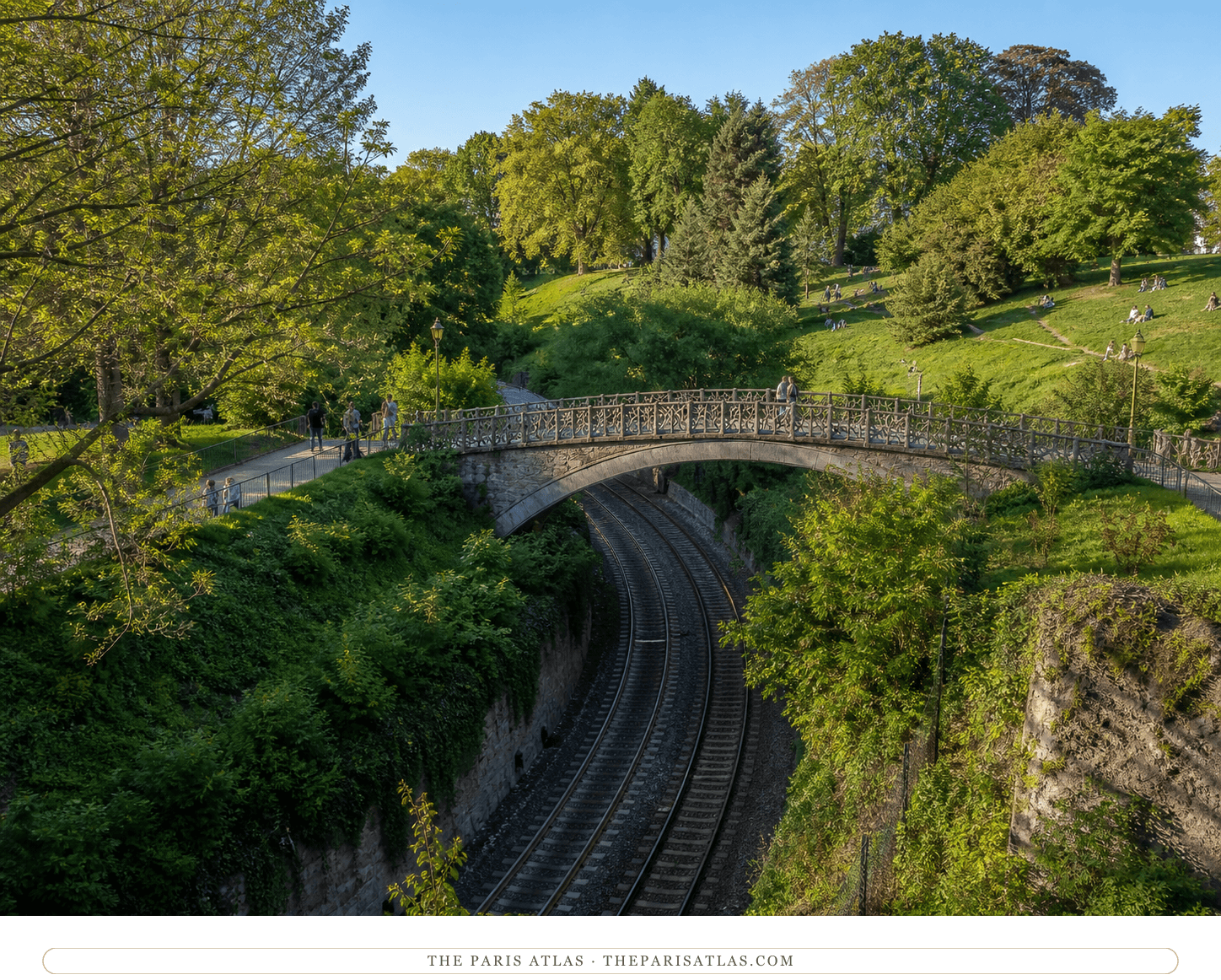 Walkers crossing a footbridge above a green railway cutting in Parc Montsouris