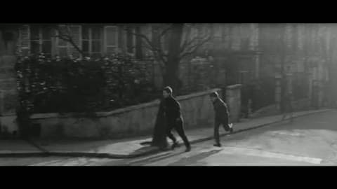 Two boys walking down a sloping Paris street lined with apartment buildings and a low wall, seen wide in black-and-white DyaliScope