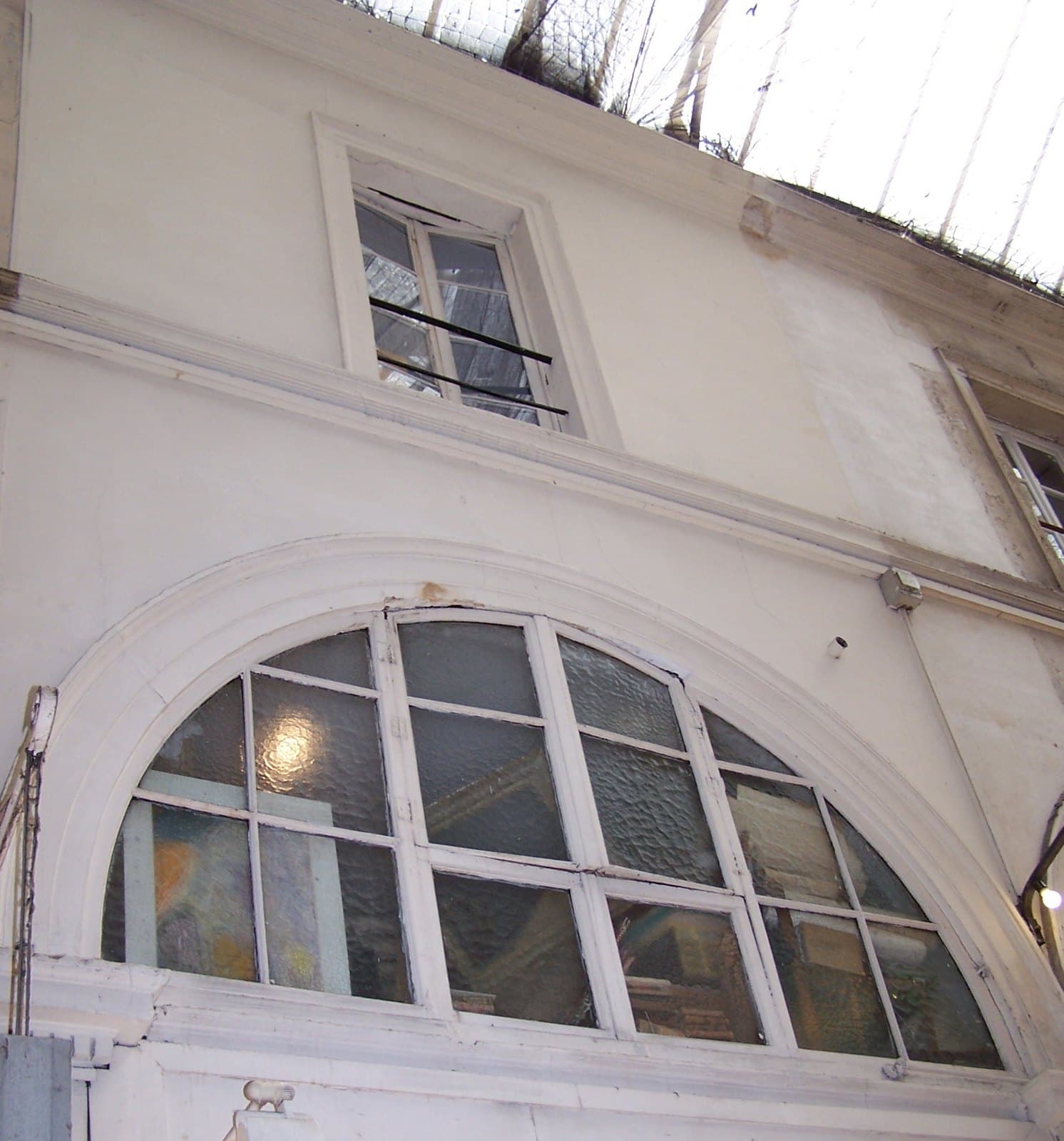 The upper storeys above number 64 in the Passage Choiseul, with the arcade's glass roof overhead