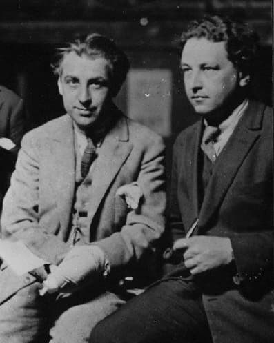 Abel Gance and Arthur Honegger seated side by side, Gance in a light suit with a bandaged hand, Honegger holding a pen