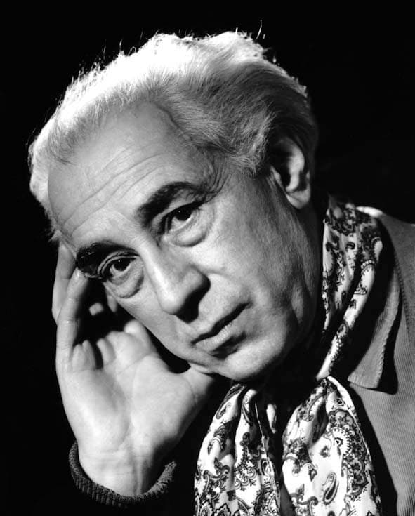 Studio portrait of Abel Gance in 1957, white-haired, head resting on one hand, wearing a paisley scarf