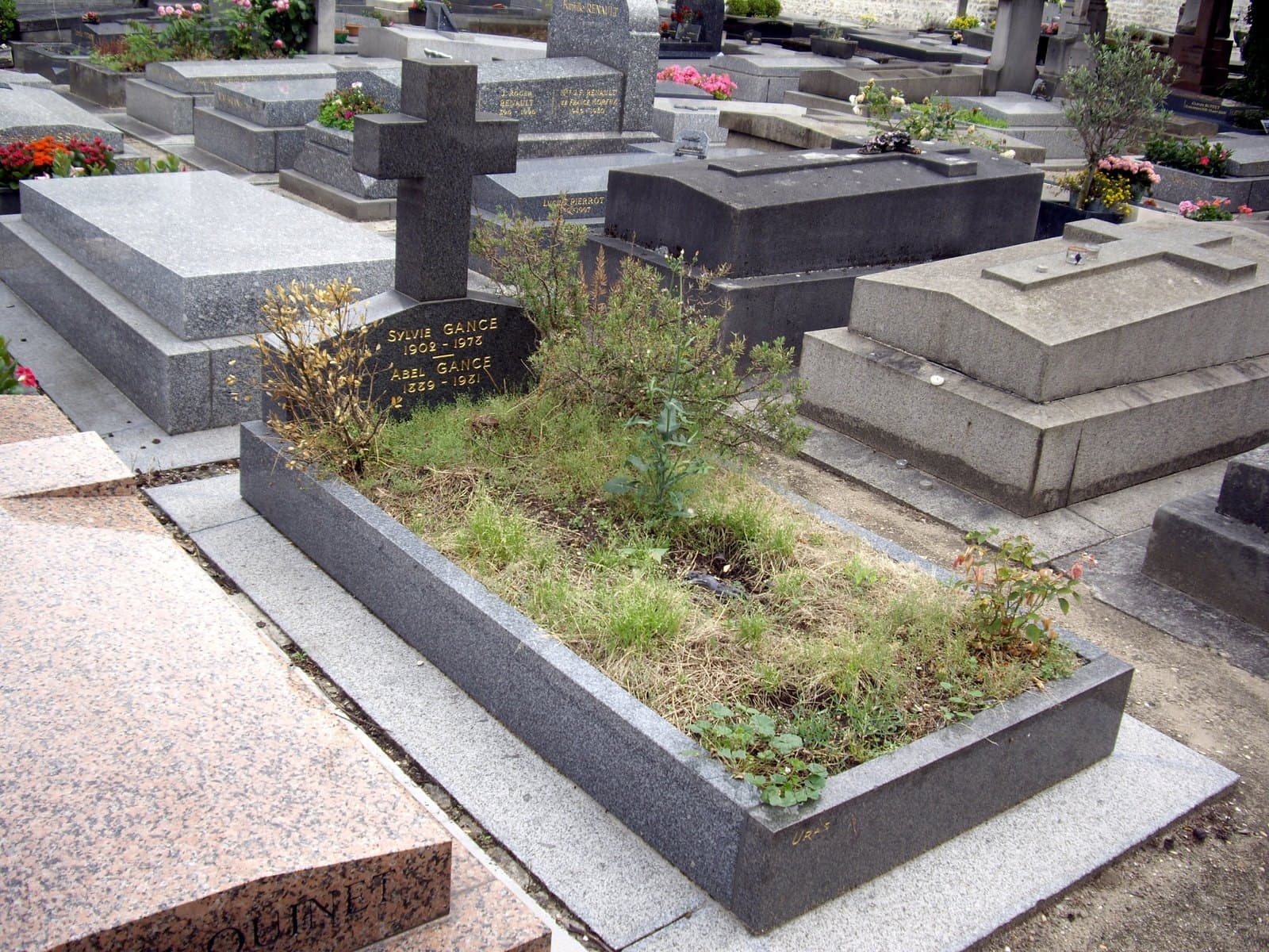 A low granite grave in a crowded cemetery, its headstone lettered in gold for Sylvie Gance and Abel Gance