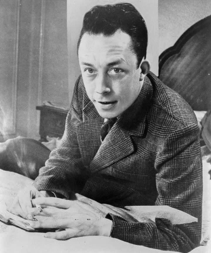 Albert Camus seated at a desk in 1957, turned in profile with a cigarette in his hand