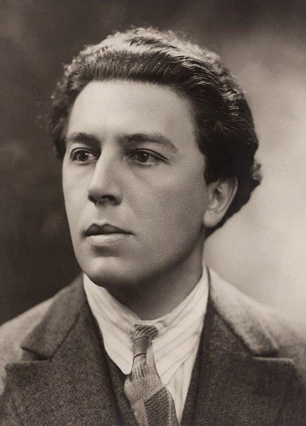 André Breton at about thirty, in three-quarter profile, wearing a tweed jacket, striped shirt, and patterned tie.