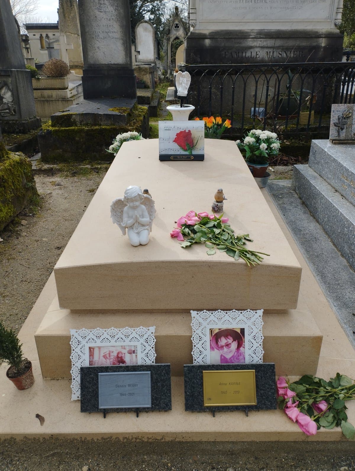 A pale stone tomb at Père-Lachaise strewn with flowers, with two nameplates and small photographs at its base