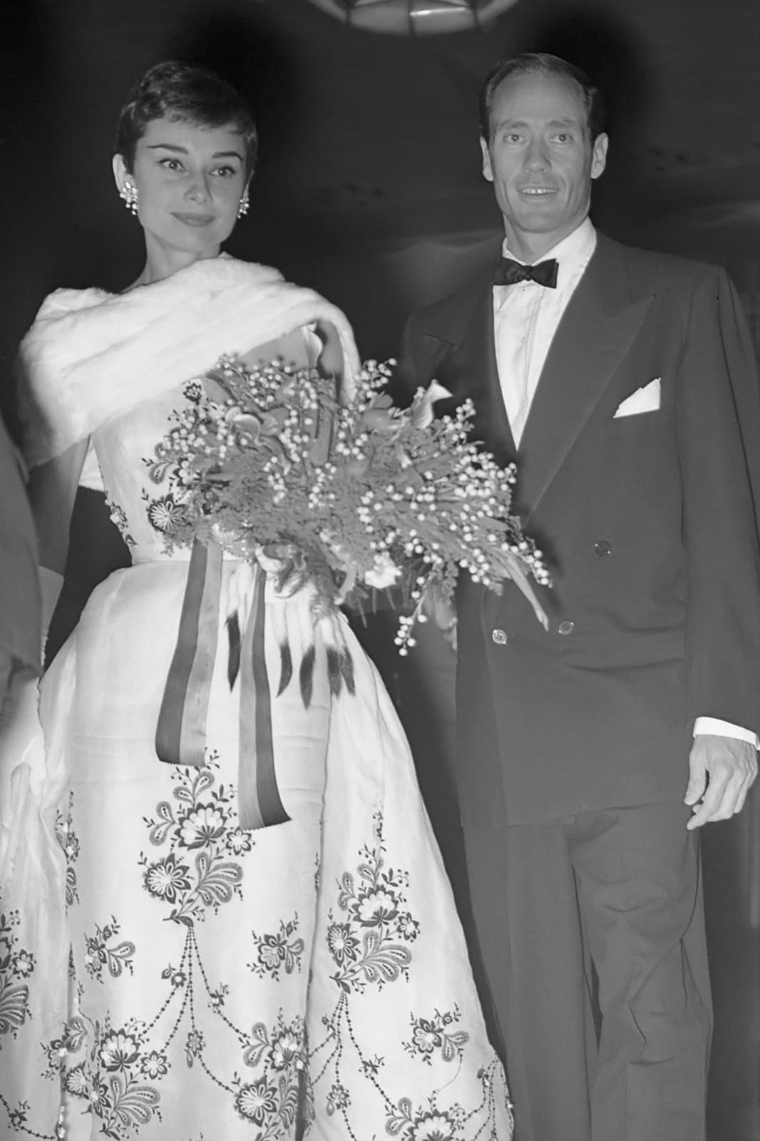 Audrey Hepburn holding flowers beside her husband Mel Ferrer at a formal film event in Amsterdam in 1954