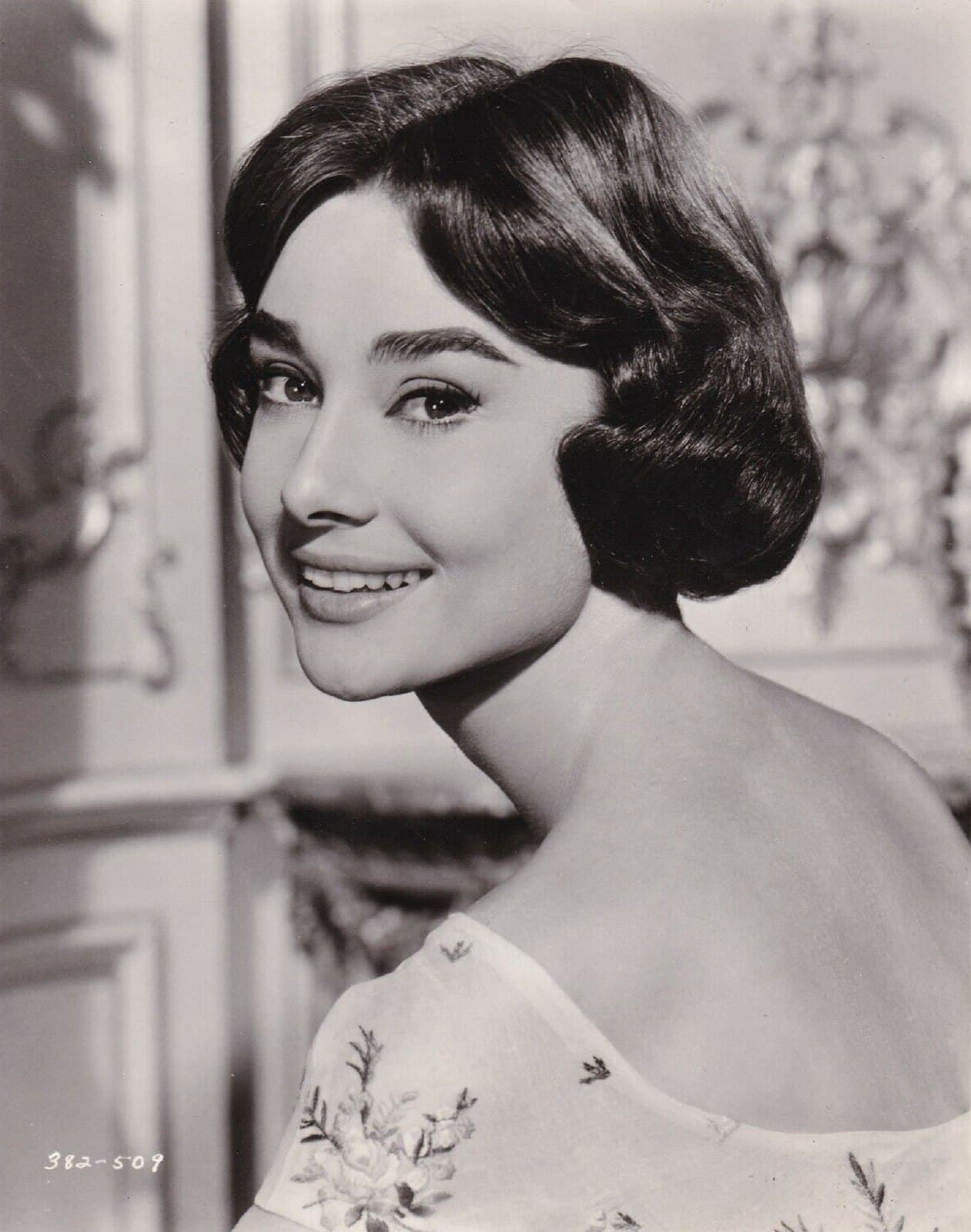 Audrey Hepburn in a 1957 black-and-white studio portrait, seated in profile and turning her face toward the camera.