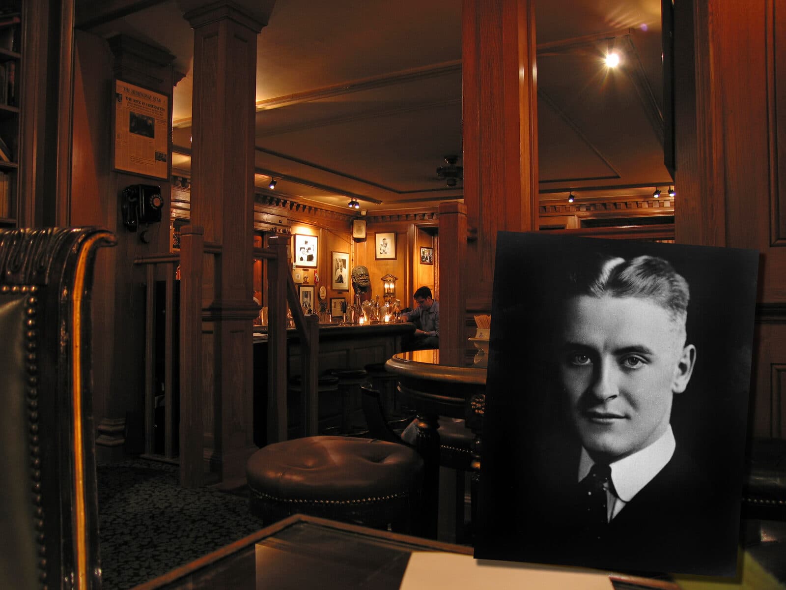 Interior of Bar Hemingway at the Hôtel Ritz — wood paneling, leather seats, a Hemingway bust, and a portrait of F. Scott Fitzgerald in the foreground