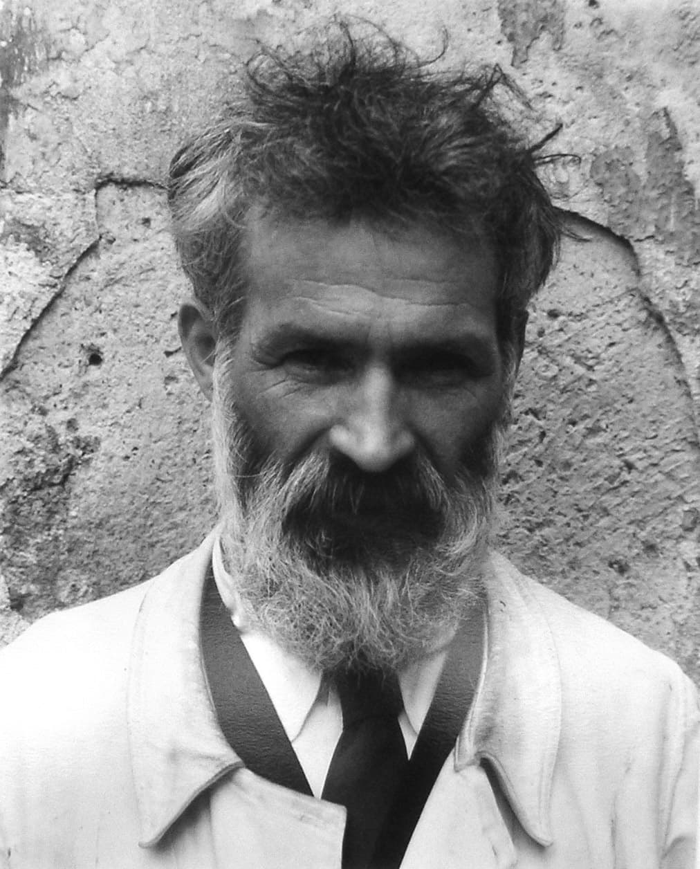 Brancusi bearded and in workman's clothes, seen in profile in his studio among pale carved forms