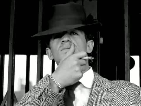 Jean-Paul Belmondo in a fedora and herringbone tweed jacket, head tilted back, dragging his thumb across his lips with a cigarette between his fingers