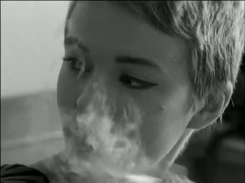 Close frame of Jean Seberg with cropped hair drawing on a cigarette, eyes glancing to the side