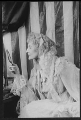 Cathleen Nesbitt in profile as Aunt Alicia, wearing a lace gown and veil and holding a hand mirror, against a striped backdrop