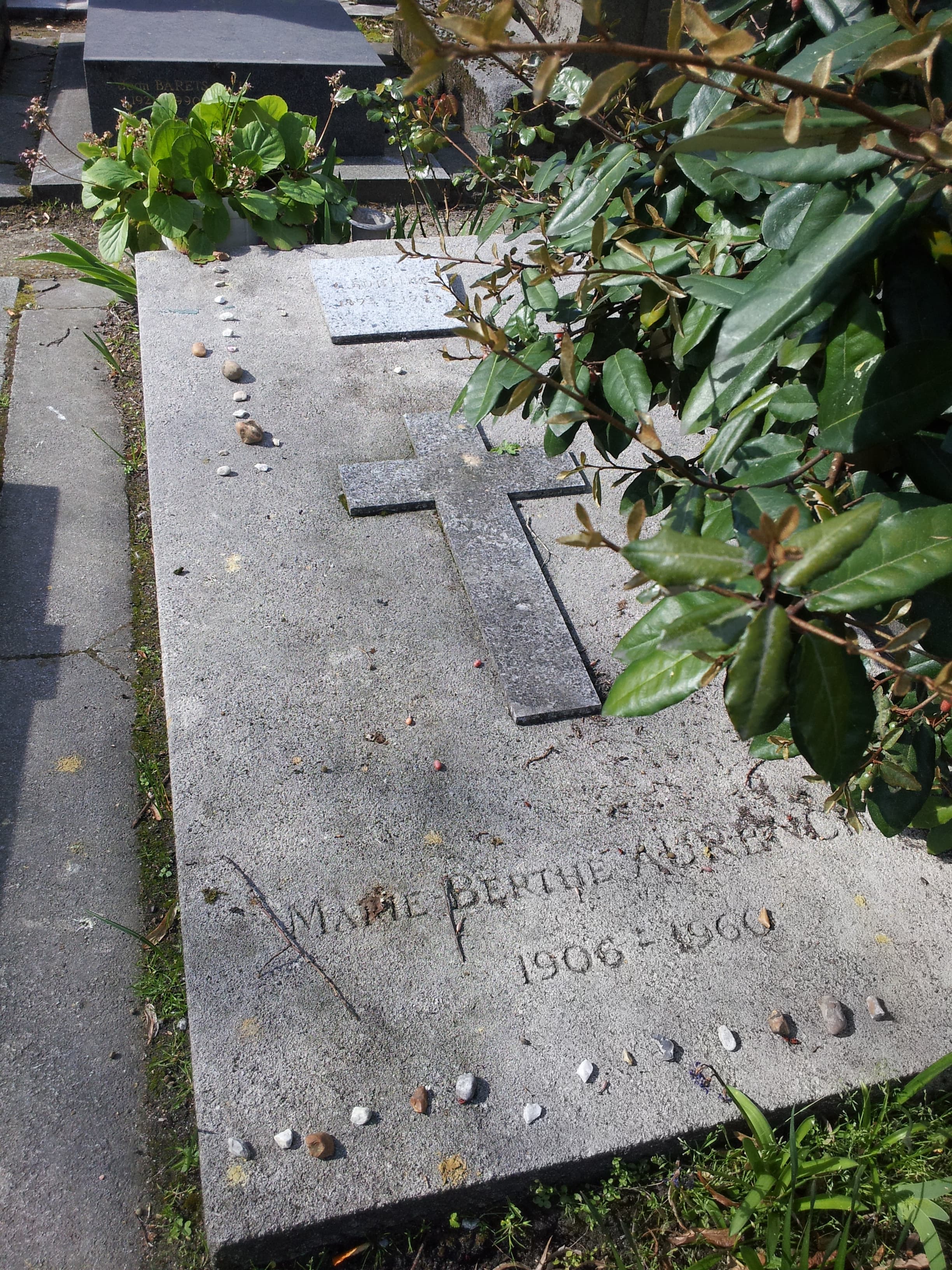 Soutine's flat grave slab at Montparnasse Cemetery with a stone cross, a small plaque, visitors' pebbles along the edges, and the carved name of Marie-Berthe Aurenche