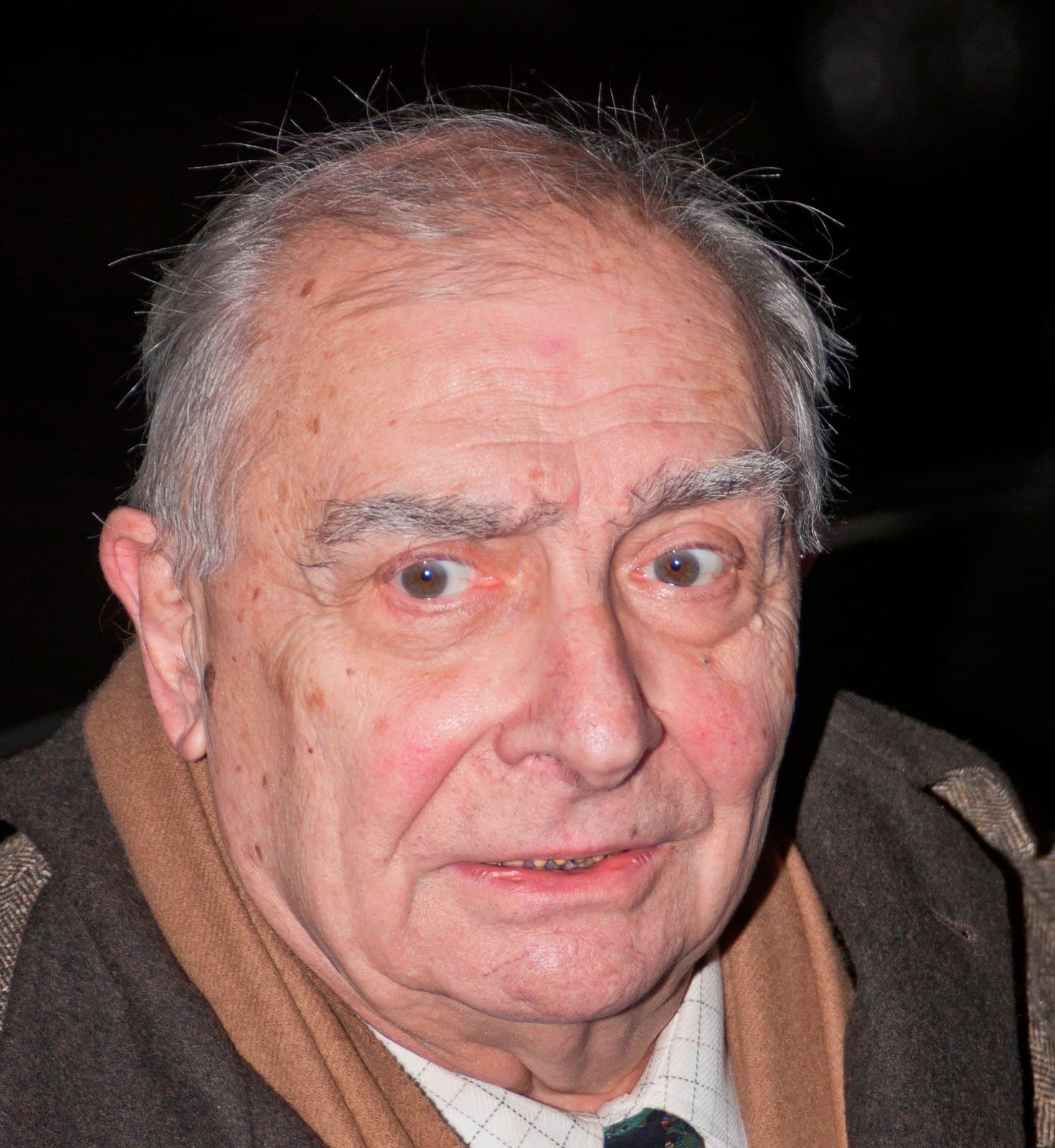 Claude Chabrol in close-up, in scarf and coat, eyebrows raised at the camera.