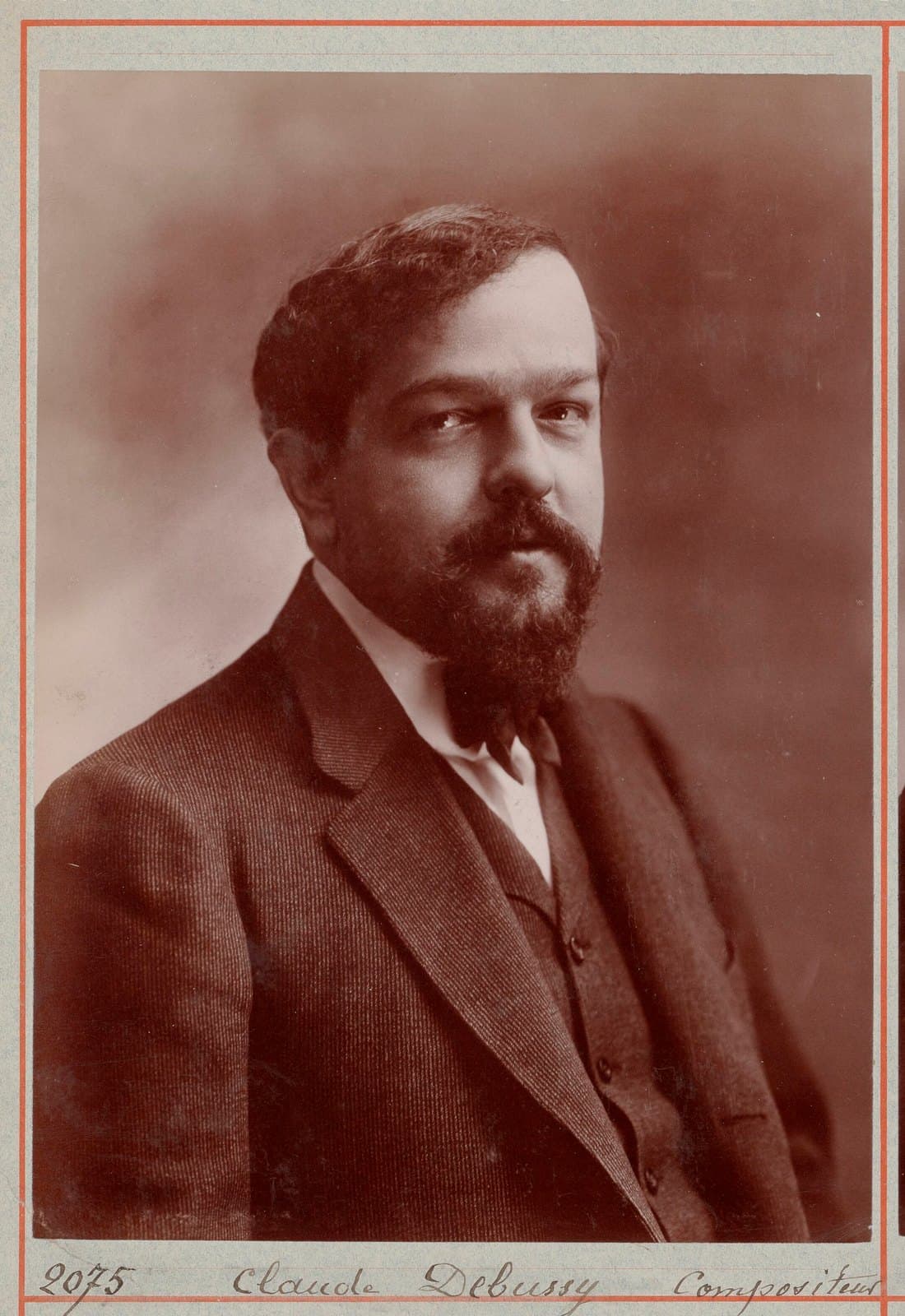 A young Claude Debussy standing in a dark suit in an Atelier Nadar portrait