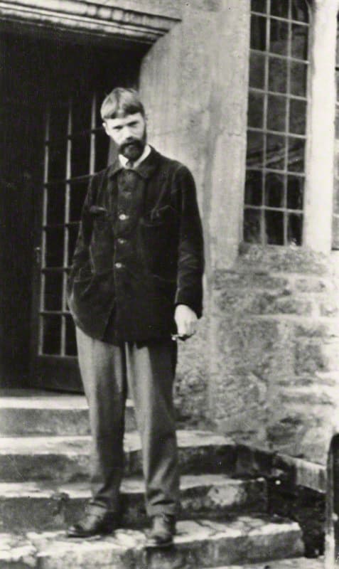 D. H. Lawrence in a corduroy jacket, standing on stone steps outside a house, photographed by Lady Ottoline Morrell in 1915.