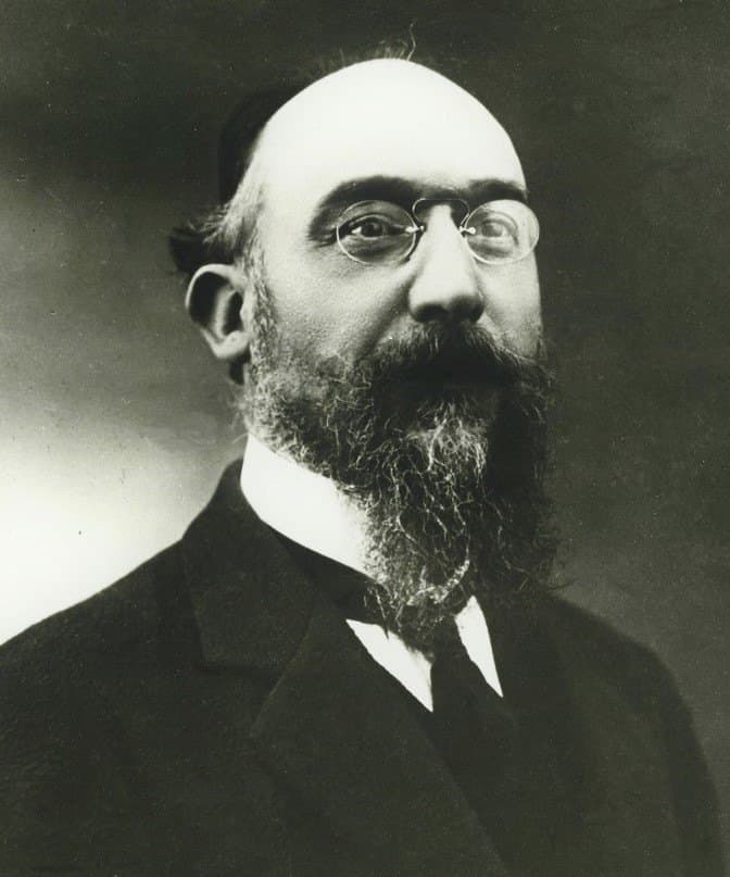 Erik Satie around 1914, in bowler hat, pince-nez, wing collar, and dark suit, looking at the camera with an umbrella at his side