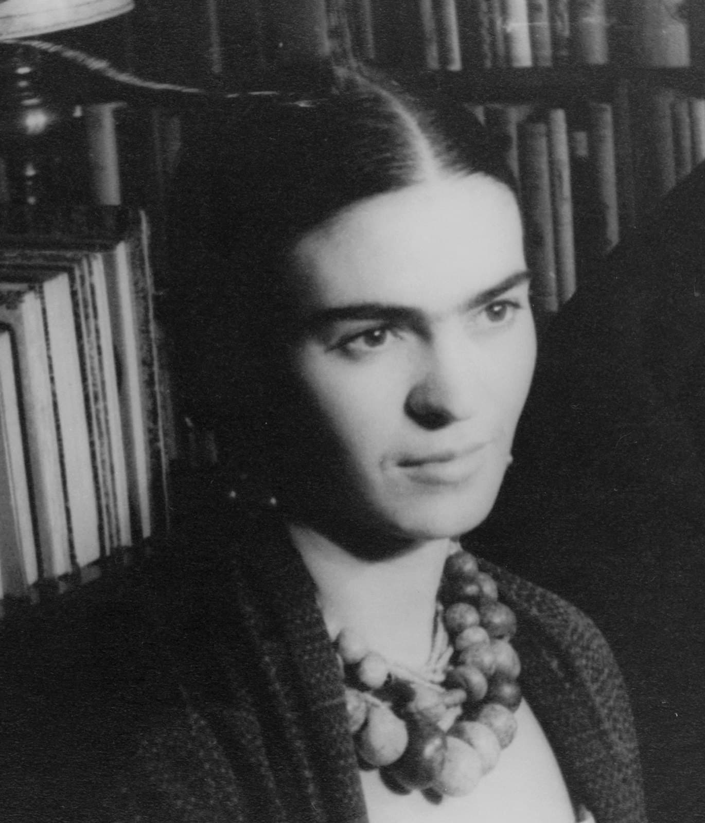 Frida Kahlo in 1932, looking directly at the camera with her hair pinned back and wearing a dark shawl and long necklace.