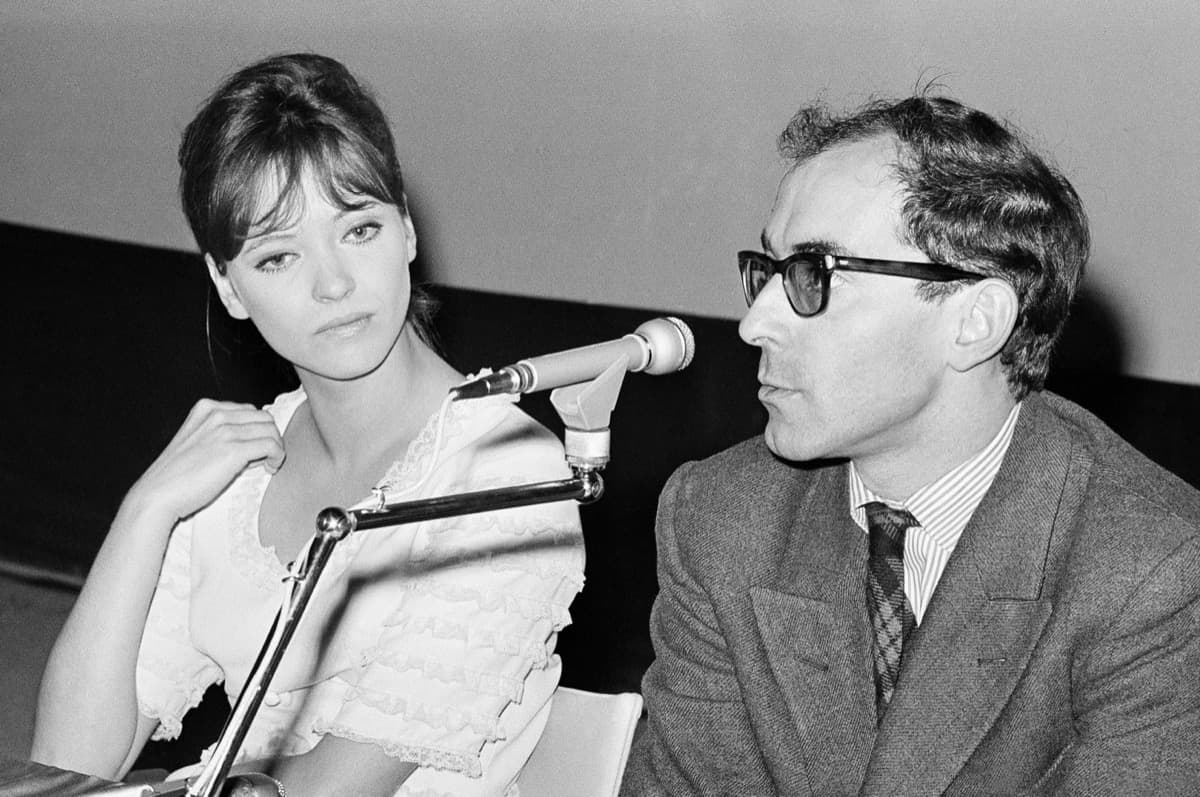Anna Karina and Jean-Luc Godard seated at a press-conference table, a microphone between them, in black and white