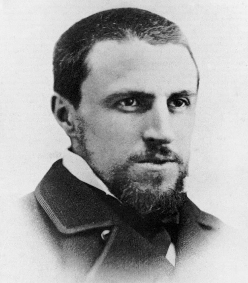 Head-and-shoulders photographic portrait of Gustave Caillebotte around age thirty: short dark hair, full beard and moustache, jacket and tie, facing the camera