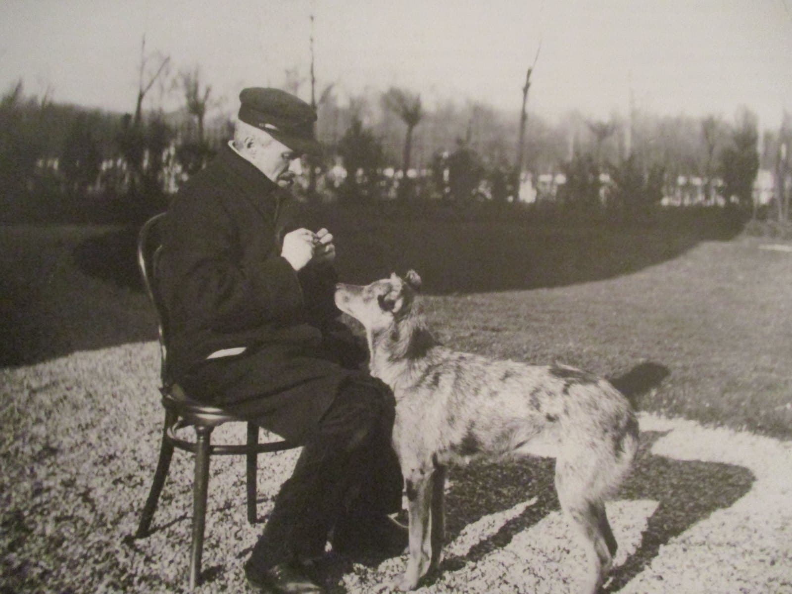Gustave Caillebotte in profile, seated outdoors in his garden with his dark long-haired dog Bergère beside him, bearded, in a heavy coat