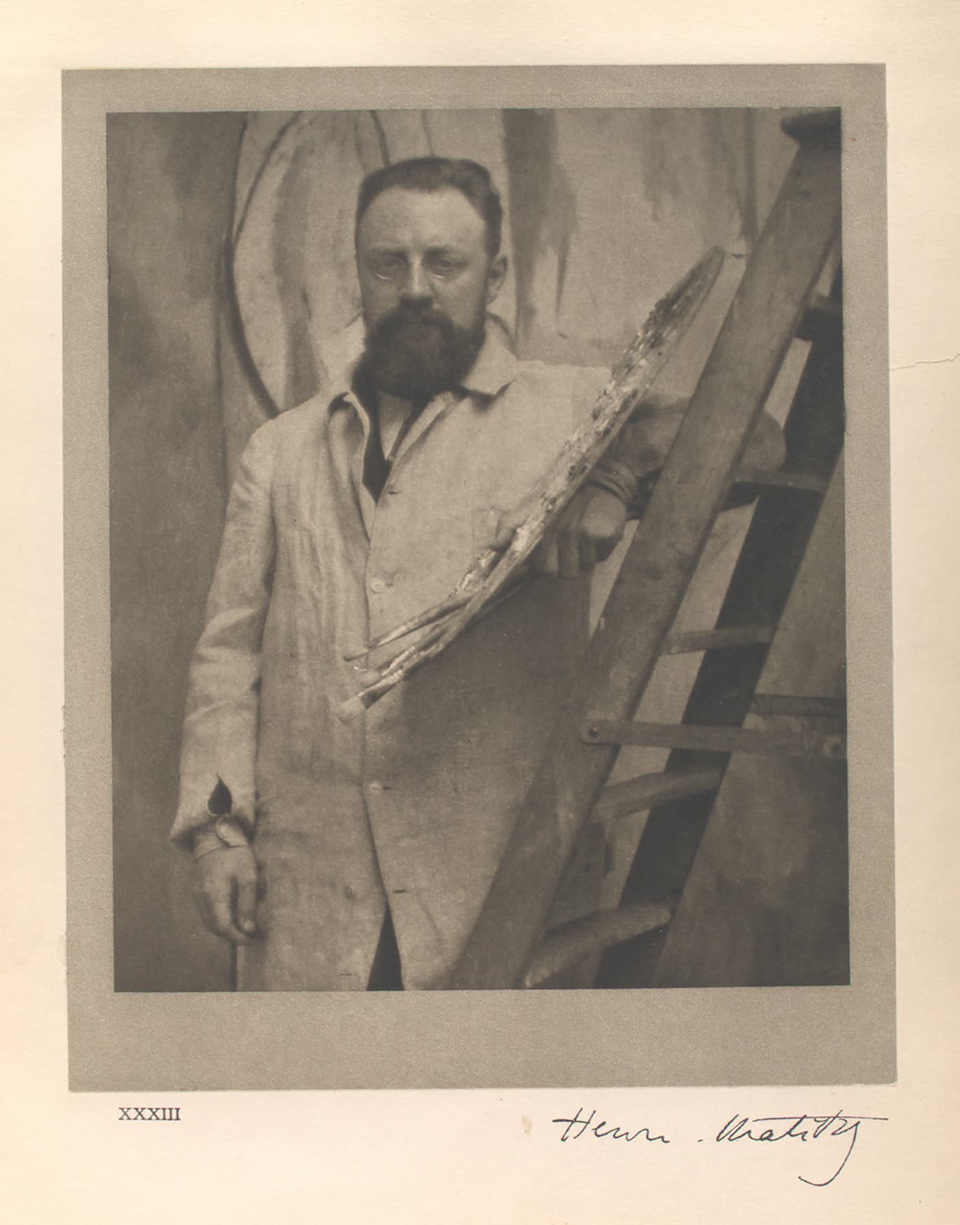 Henri Matisse standing at an easel in his studio, brush in hand, wearing a suit, a large canvas on the easel beside him