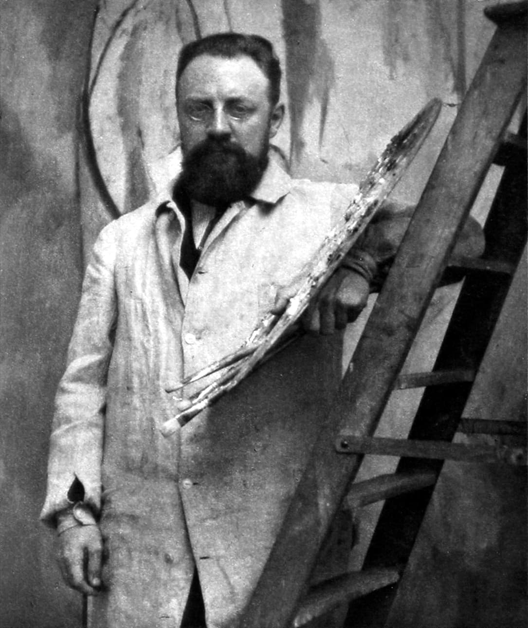 Henri Matisse at forty-three, bearded and in glasses, seated and looking at the camera with his hands folded