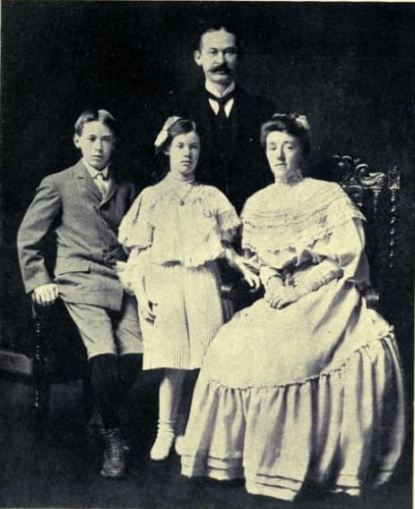 Studio portrait of the Miller family: young Henry seated at left in a suit, his sister standing at center, his mother seated in a white dress, his father standing behind.