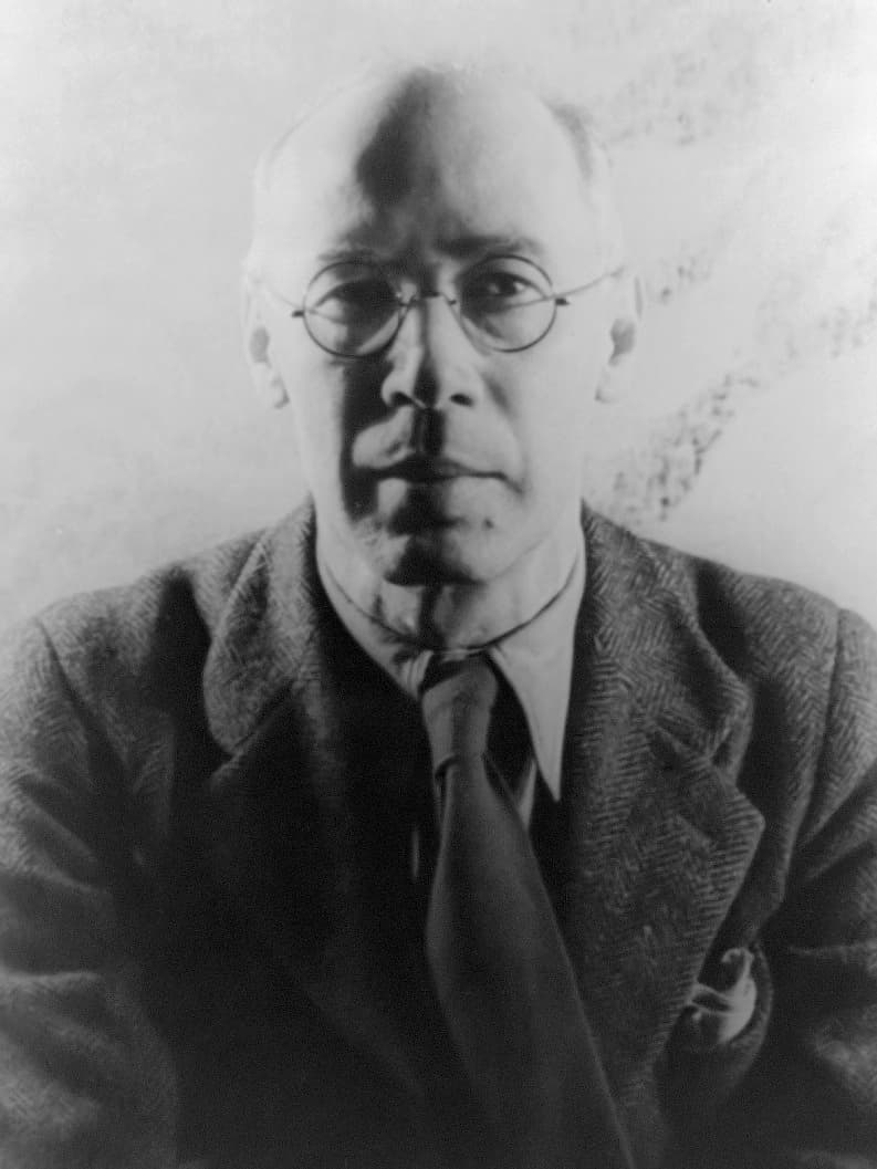 Henry Miller facing the camera in round glasses, tweed jacket, and tie.