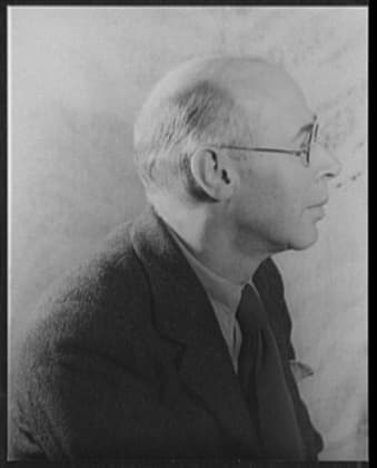 Henry Miller in profile, bald with round glasses, in a tweed jacket.