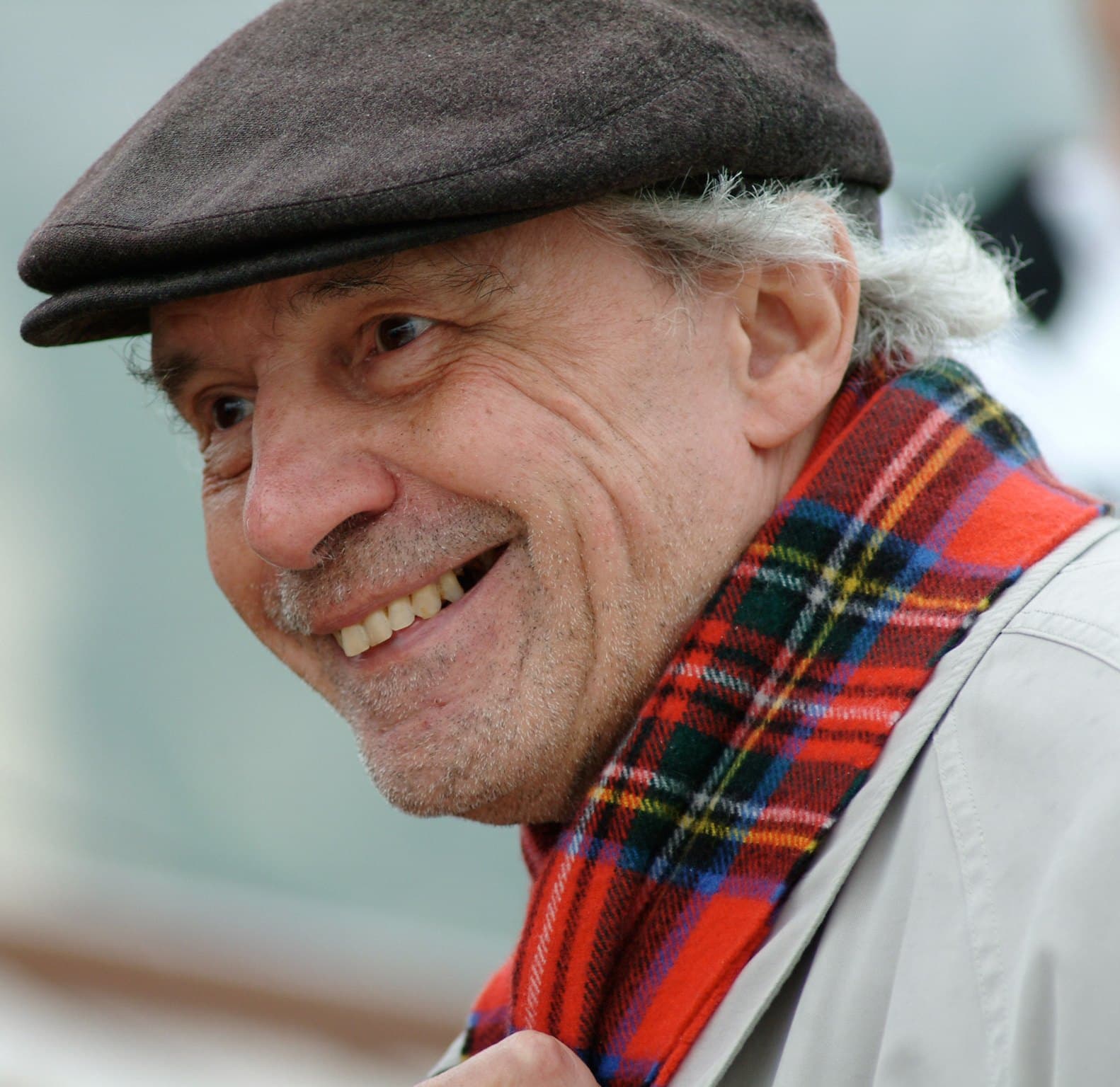 Jacques Rivette smiling in a flat cap and red tartan scarf.