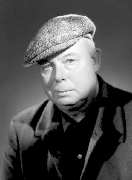 Studio portrait of Jean Renoir in 1955, in a suit, lit in the Harcourt house style
