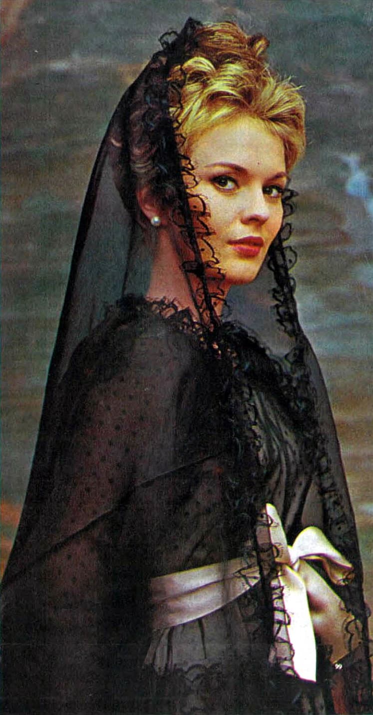 Color magazine photograph of Jean Seberg in a black lace mantilla veil and dress with a white sash, looking over her shoulder