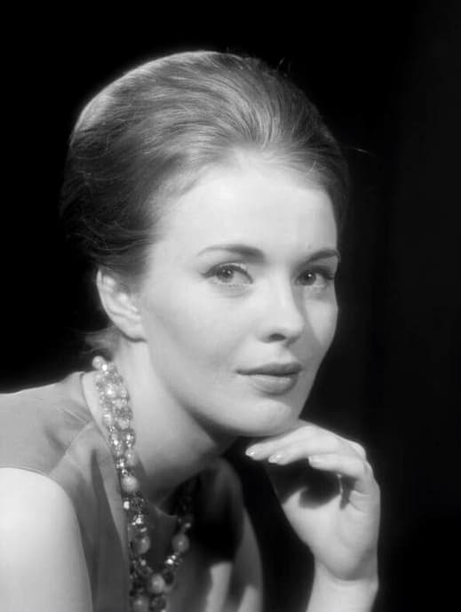Studio portrait of Jean Seberg in 1961: swept-up hair, beaded necklace, chin resting on her hand against a dark background