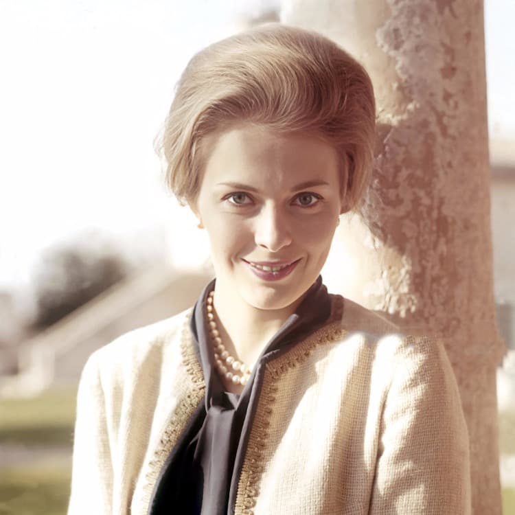 Color photograph of Jean Seberg smiling beside a stone column in Venice, wearing pearls and a cream jacket