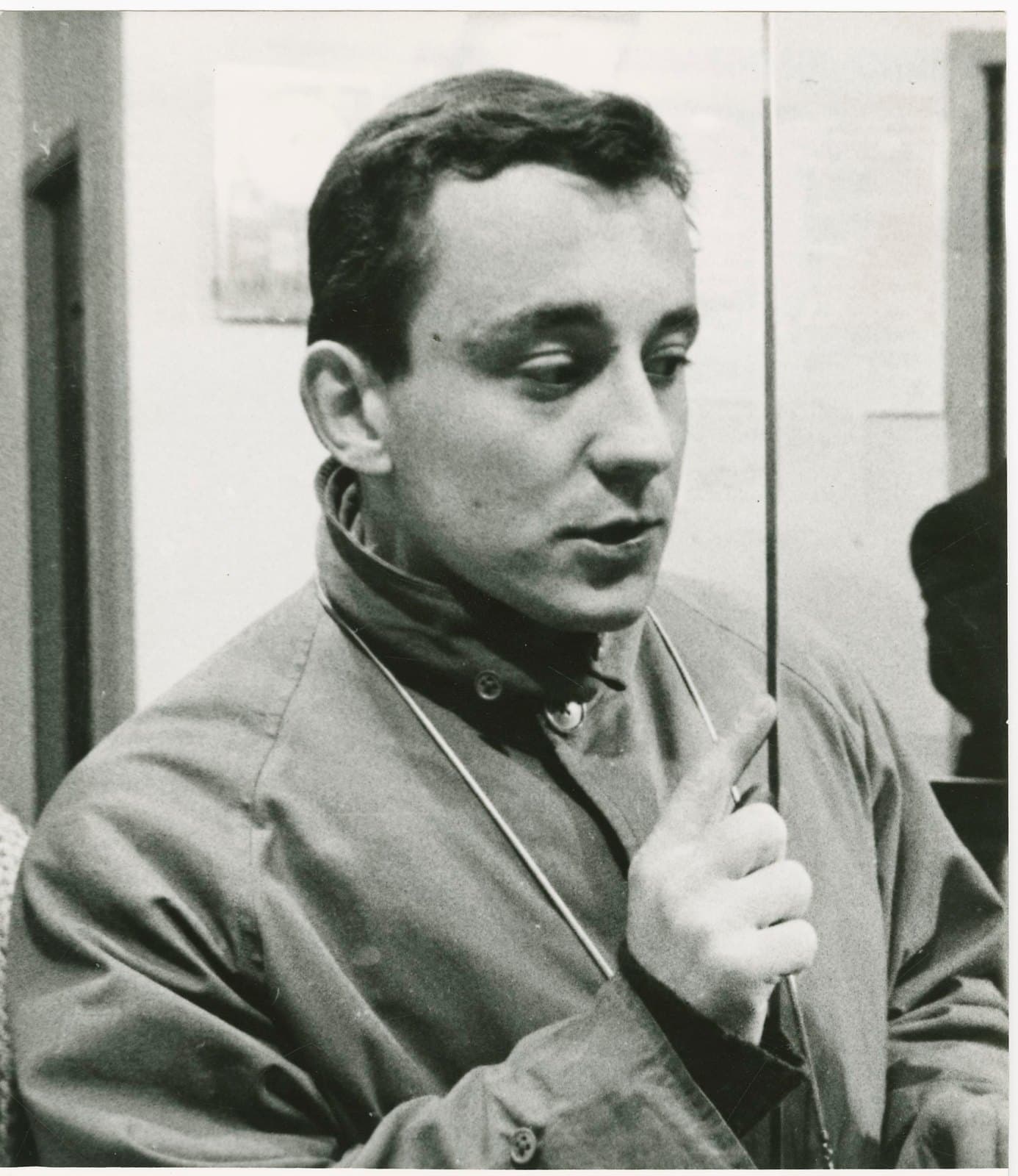 Louis Malle at twenty-six in a raincoat, caught mid-sentence with a raised finger.