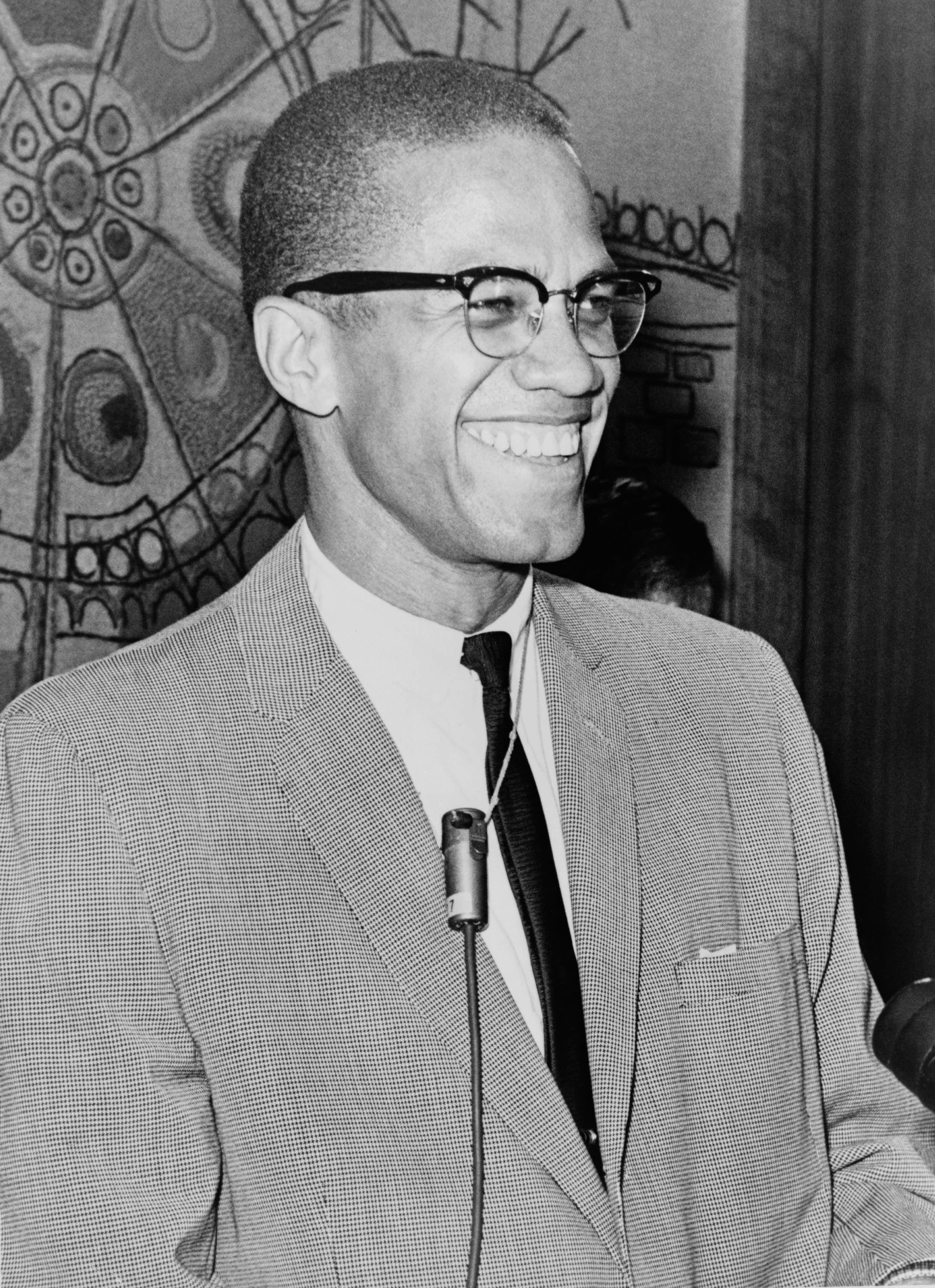 Half-length portrait of Malcolm X facing right, wearing a suit and glasses.