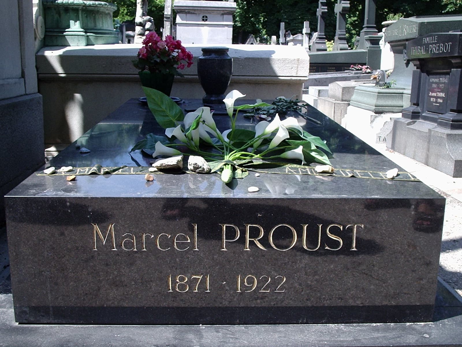 Proust's black granite tomb at Père Lachaise, engraved Marcel Proust 1871–1922, with flowers and visitors' pebbles on the slab.