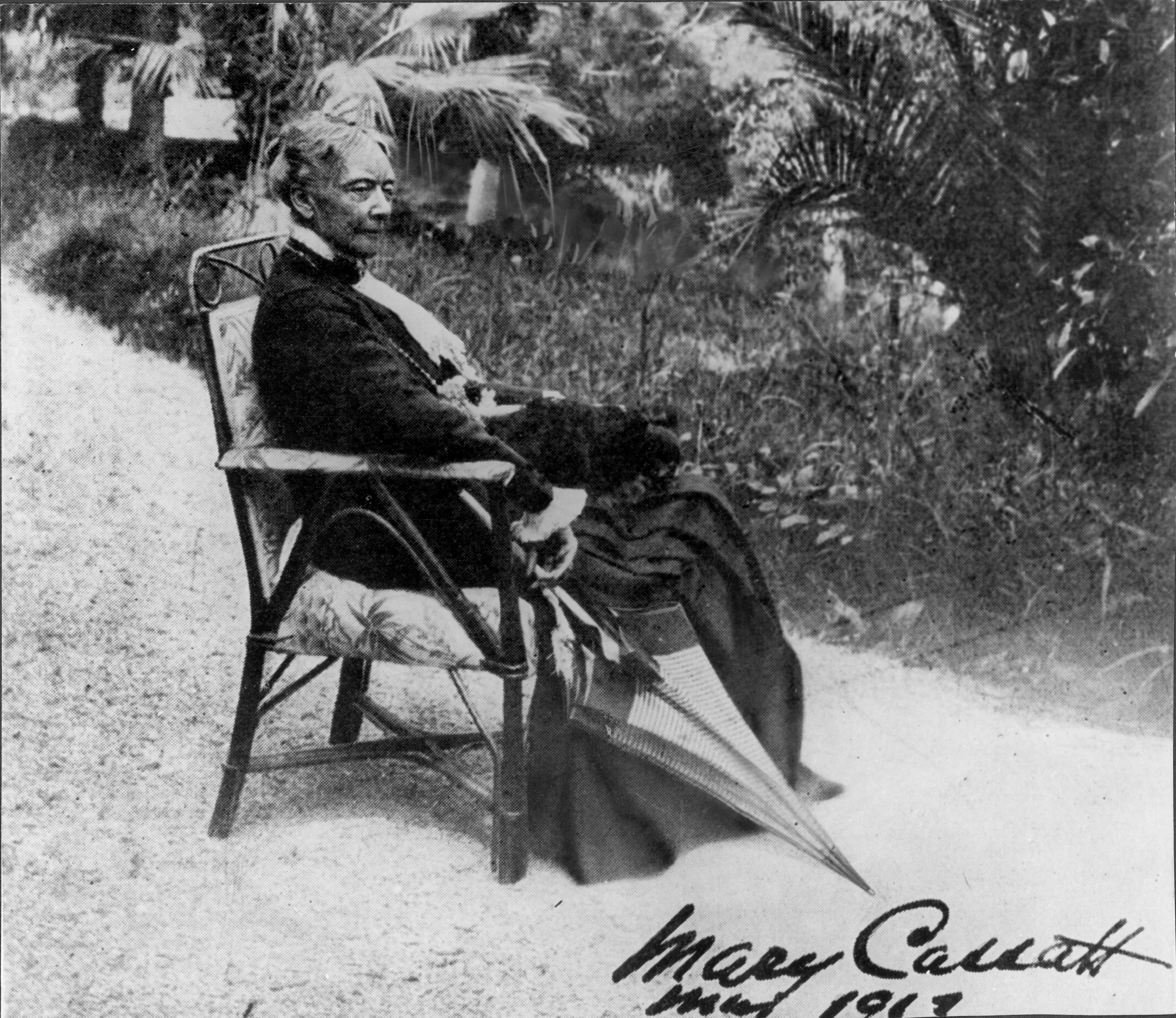 Mary Cassatt at sixty-nine, seated outdoors in a dark coat and wide hat, her hands folded, looking directly at the camera