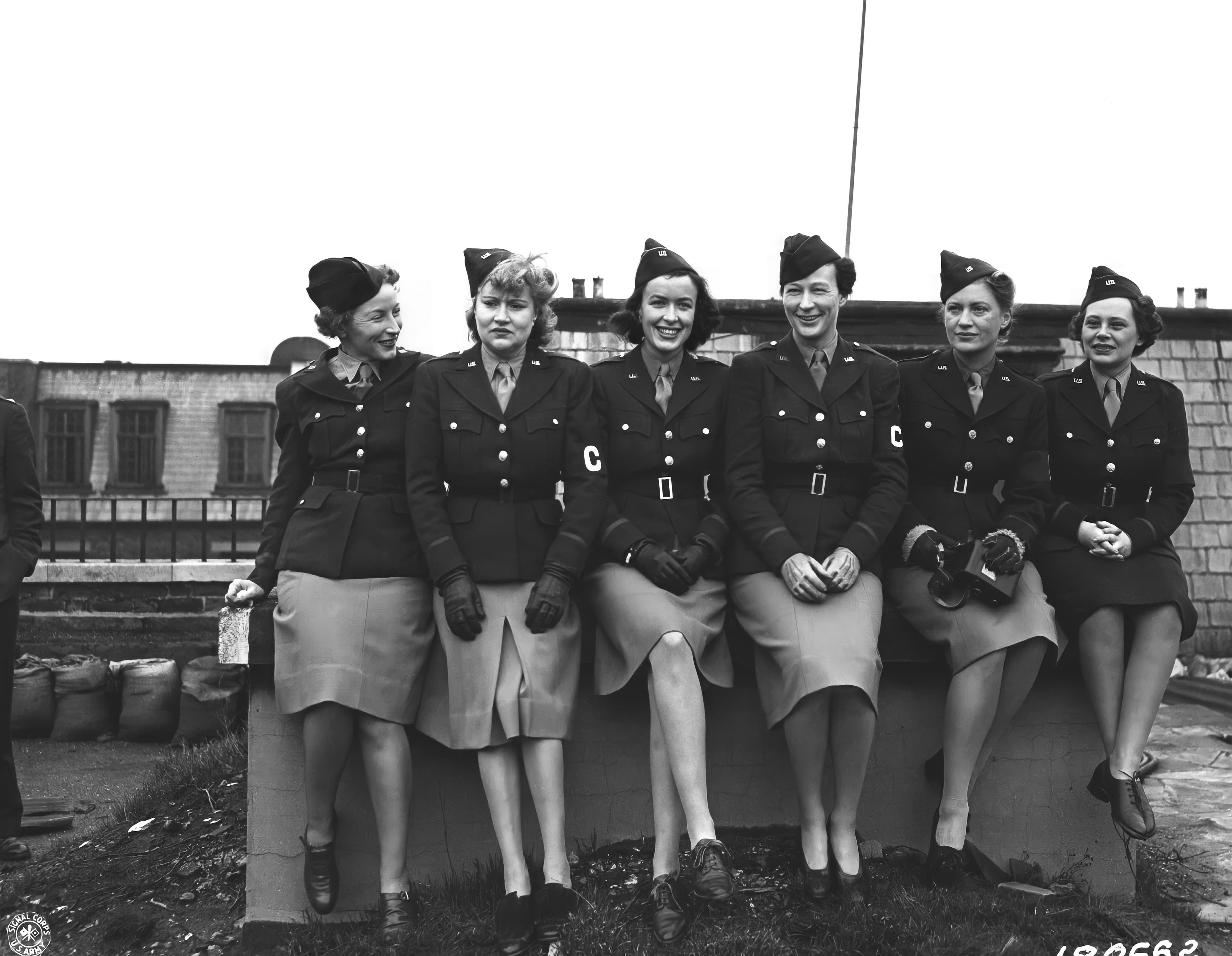 Six women war correspondents in U.S. Army uniform seated on a wall, 1943
