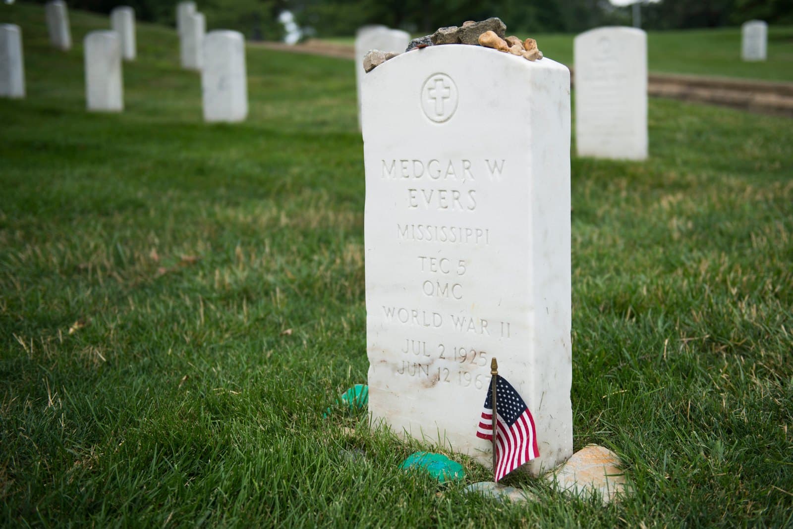 Medgar Evers's white marble military headstone at Arlington National Cemetery, topped with remembrance stones and marked by a small United States flag