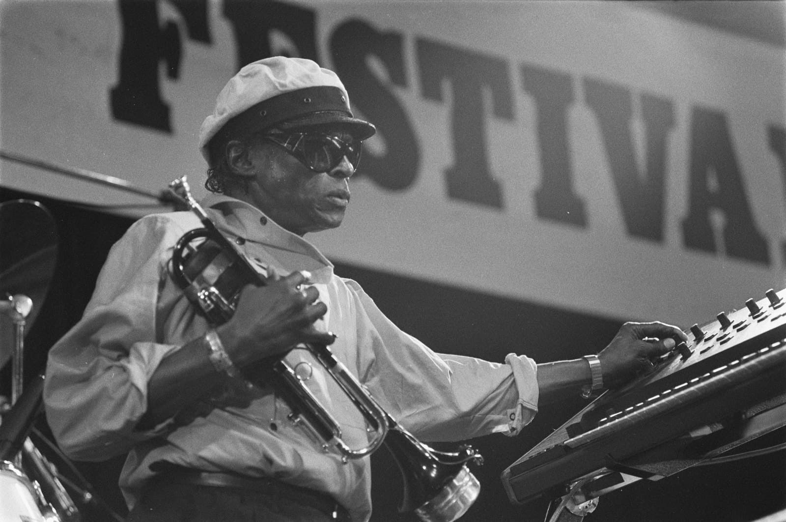 Miles Davis holding his trumpet while adjusting electronic equipment onstage at the North Sea Jazz Festival in 1984