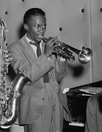 Miles Davis in a dark suit holding his trumpet at the Three Deuces jazz club in New York in 1947
