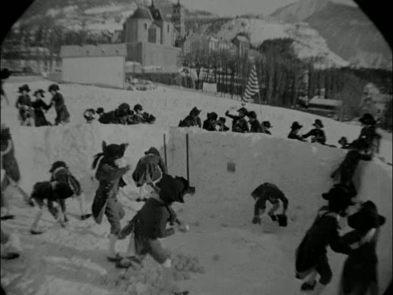 Wide iris-framed shot of schoolboys battling from snow forts at Brienne, a snow-covered village and church behind them