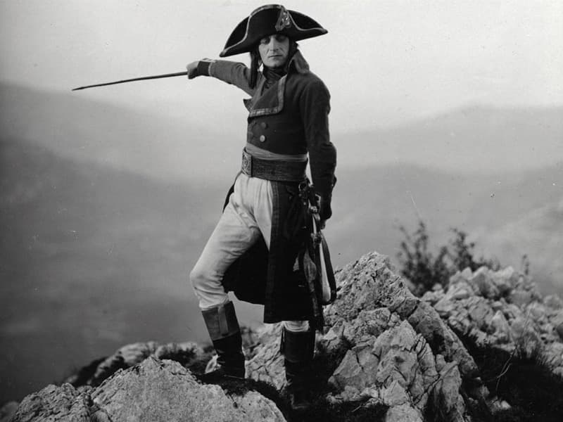 Albert Dieudonné in bicorne and uniform standing on a rocky outcrop, arm outstretched, hills fading into mist behind him