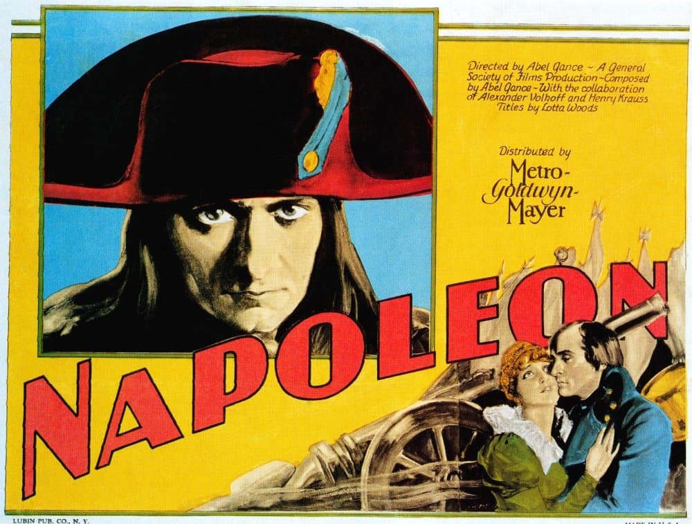 Color 1929 American poster for Napoleon: Dieudonné's face under a red bicorne beside bold red lettering, with Napoléon embracing Joséphine by a cannon wheel